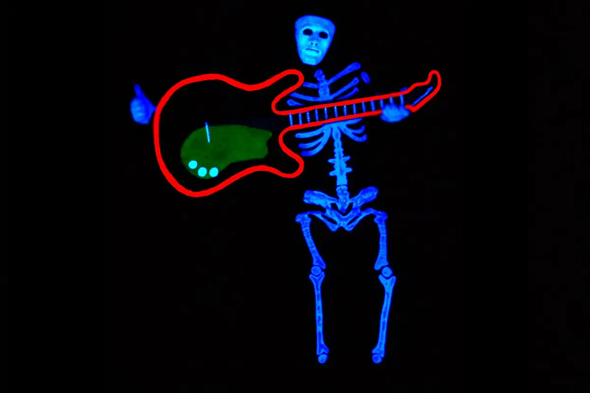 Et glødende blåt skelet med en hvid maske spiller på en klart rød guitar i mørket